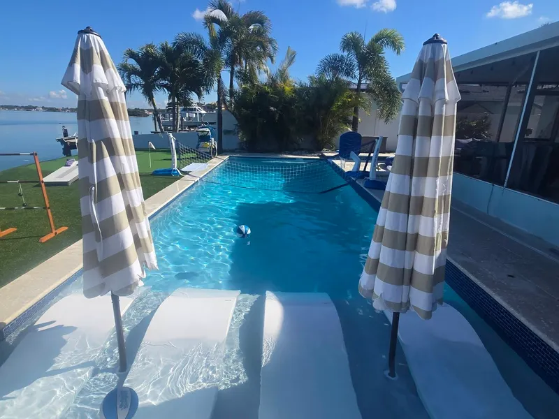 A clean waterfront pool with in-pool loungers and umbrellas
