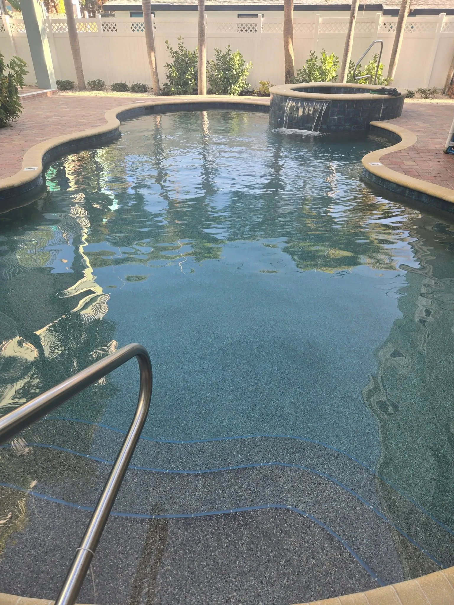 A clean backyard pool with a raised spa and waterfall feature on brick pavers