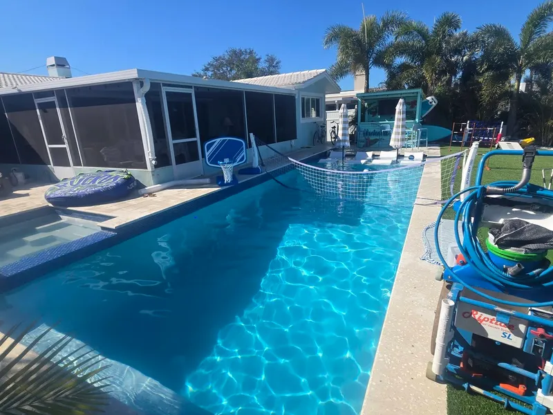 A professional Riptide pool vacuum beside a clean backyard pool