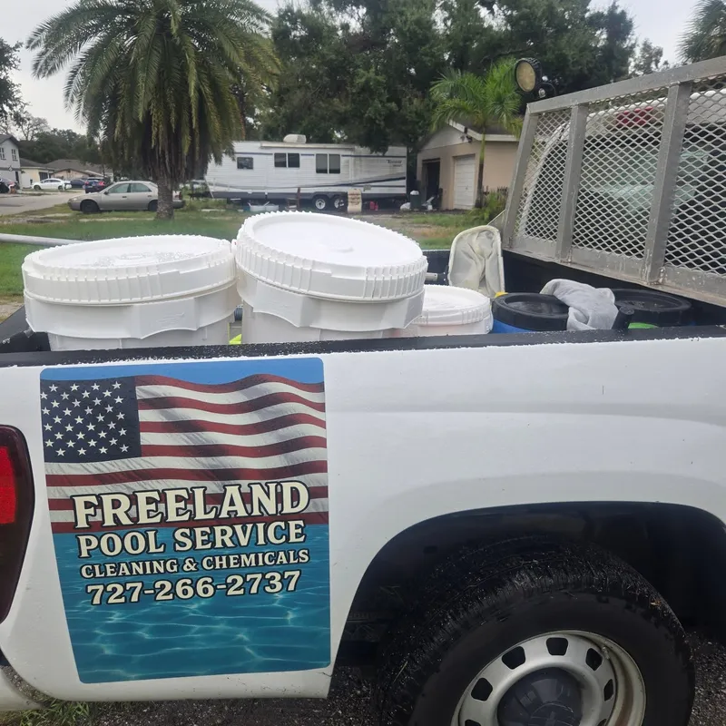 The Freeland Pool Service truck, loaded with chemical buckets, with the American flag logo and phone number on the side